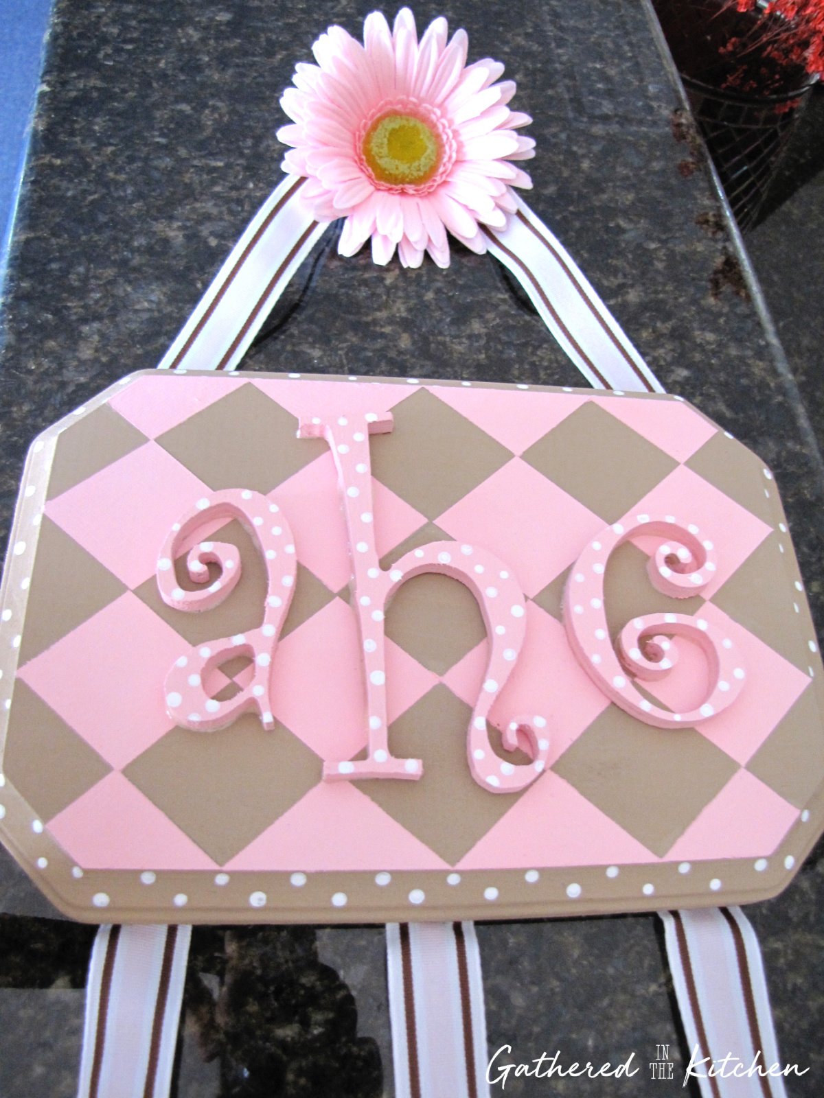 A completed DIY hair bow holder with a personalized name plaque, ribbon hangers, and a pink flower decoration. | Gathered In The Kitchen