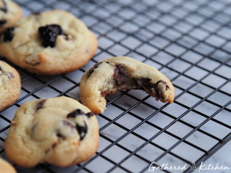 Soft cherry almond chocolate chip cookie with a bite taken out showing melted chocolate and dried cherries