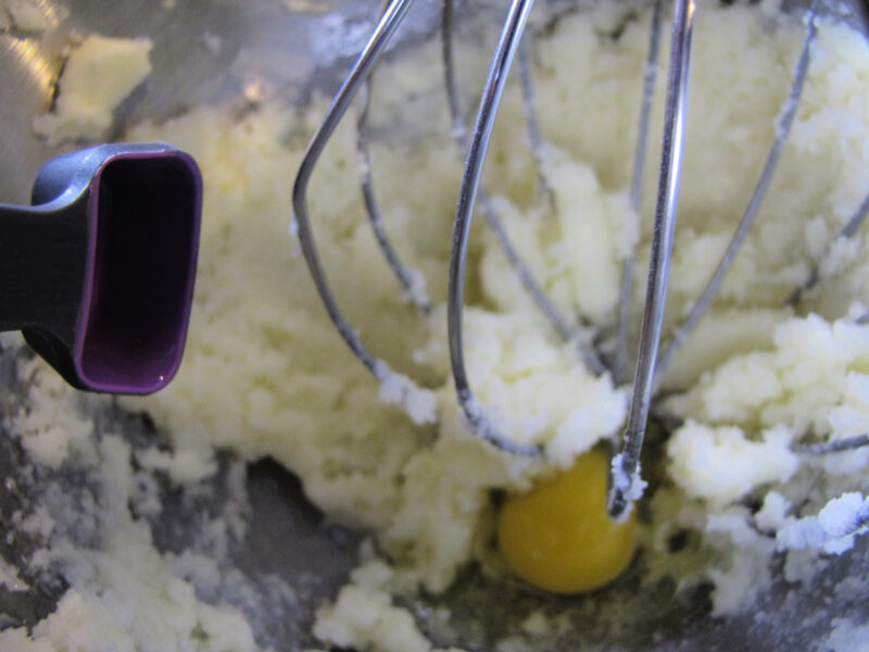 Egg being added to butter and sugar mixture while making cherry almond chocolate chip cookie dough. | Gathered In The Kitchen 