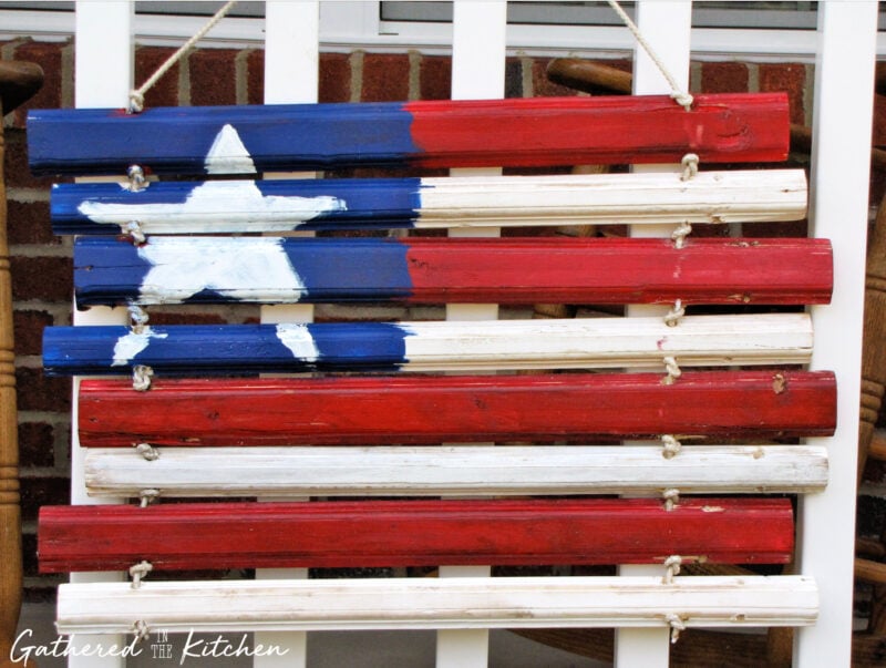 Rustic American flag door hanging made from painted scrap wood slats and rope, featuring red, white, and blue stripes with a hand-painted star design for patriotic porch decor | Gathered In The Kitchen