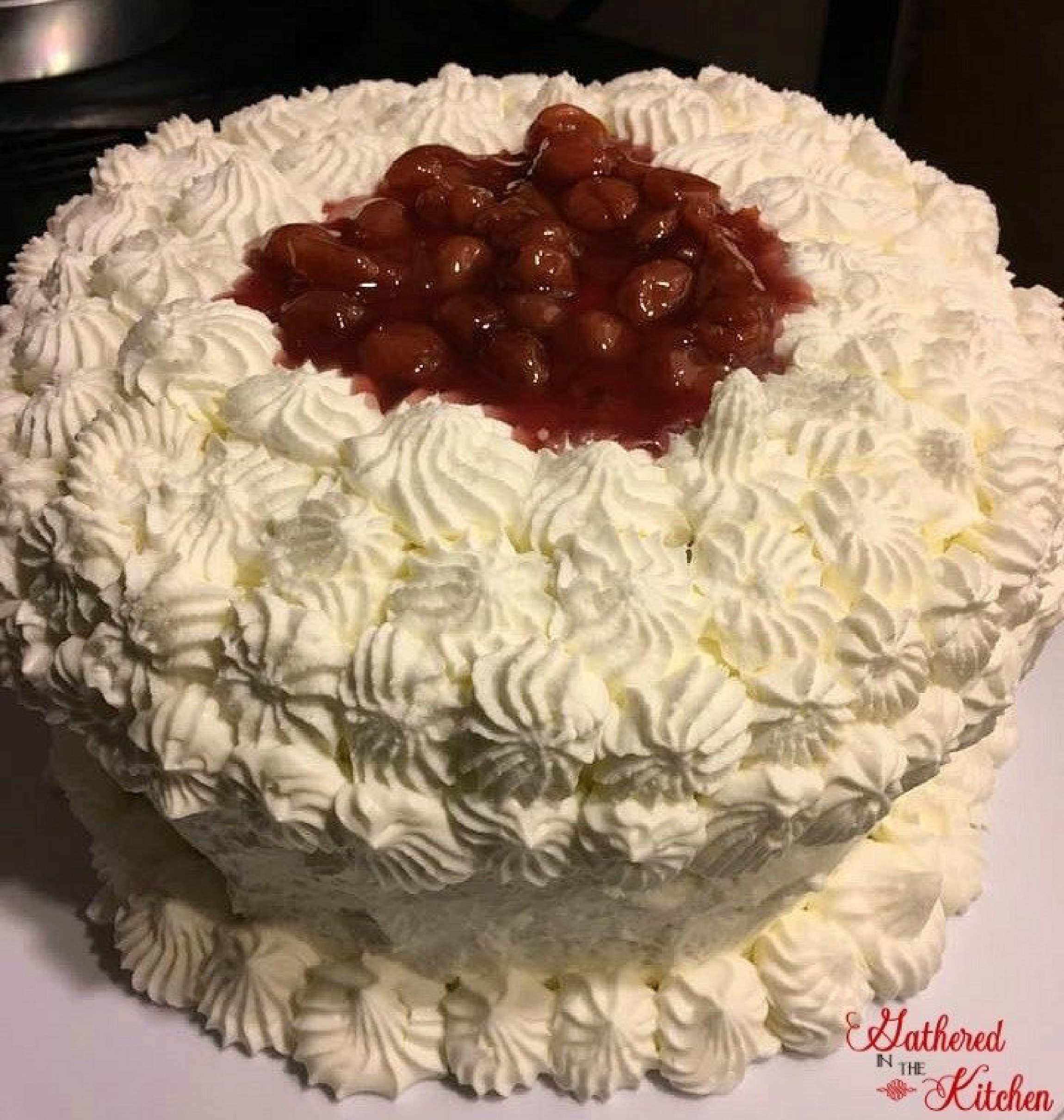 A homemade German Black Forest Cake covered in piped whipped cream and topped with a cherry filling, showcasing its elegant decoration and rich flavors. | Gathered In The Kitchen