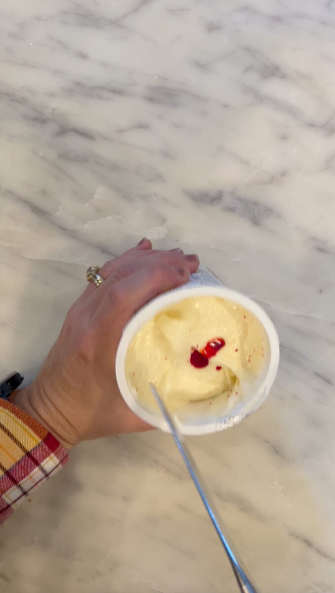 Mixing red food coloring into cream cheese frosting to create orange icing for pumpkin-shaped mini bundt cakes. | Gathered In The Kitchen 