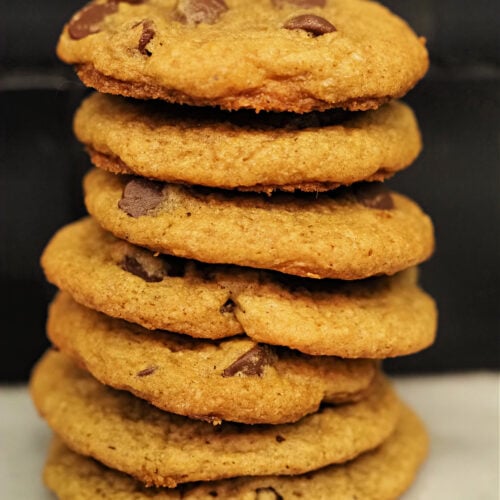 A tall stack of chewy pumpkin chocolate chip cookies with golden edges and gooey chocolate chips, photographed close-up on a marble surface. | Gathered In The Kitchen