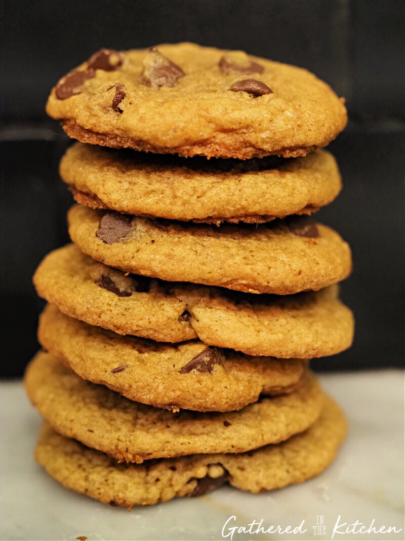 A tall stack of chewy pumpkin chocolate chip cookies with golden edges and gooey chocolate chips, photographed close-up on a marble surface. | Gathered In The Kitchen 