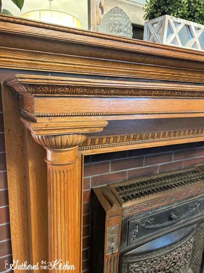 Close-up of an ornate vintage oak fireplace mantel with carved trim and fluted column detail, restored on a 1906 Aldine fireplace in an 1886 Victorian home. | Gathered In The Kitchen 