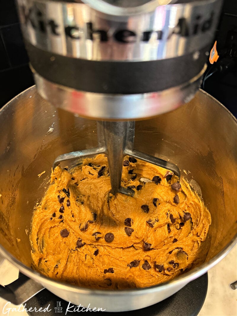 A mixing bowl of pumpkin chocolate chip cookie dough in a stand mixer, showing the rich, spiced dough flecked with chocolate chips before baking. | Gathered In The Kitchen 