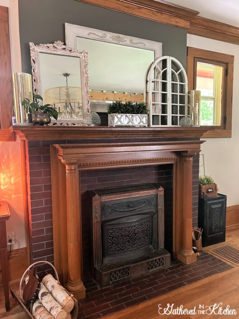 Restored 1906 Aldine fireplace in an 1886 Victorian home with a vintage oak mantel, decorative mirrors, greenery, and rustic accents styled on the mantelpiece. | Gathered In The Kitchen
