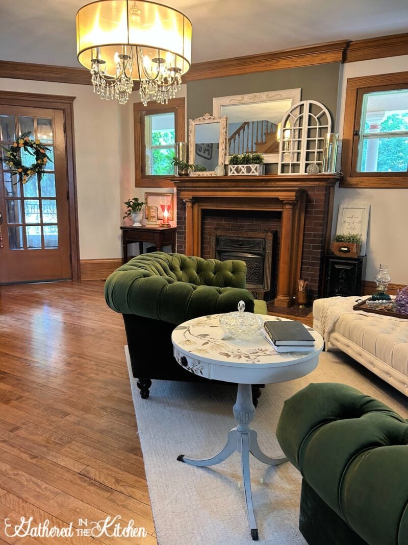 Victorian living room with restored 1906 Aldine fireplace, vintage oak mantel, green tufted sofas, chandelier, and cozy historic-inspired decor. | Gathered In The Kitchen 