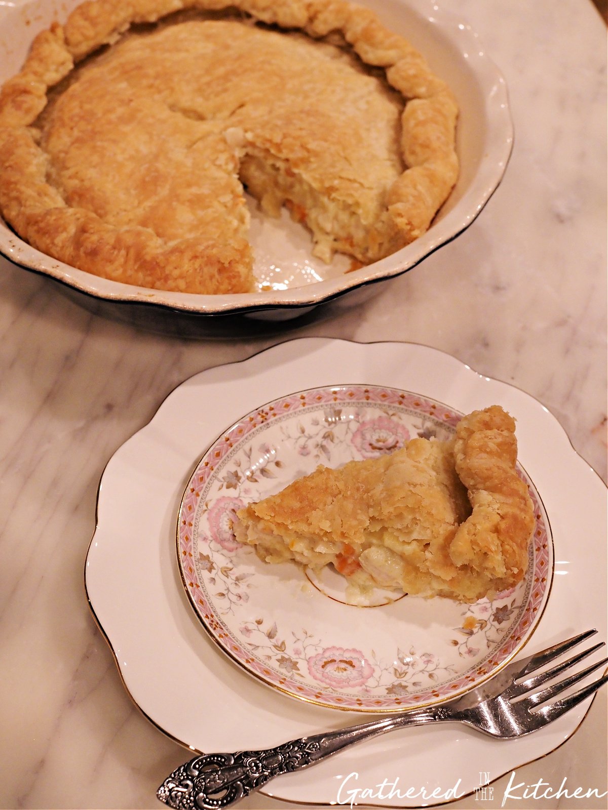 Slice of homemade chicken pot pie on a decorative plate with a fork, with the remaining pie in the background. | Gathered In The Kitchen