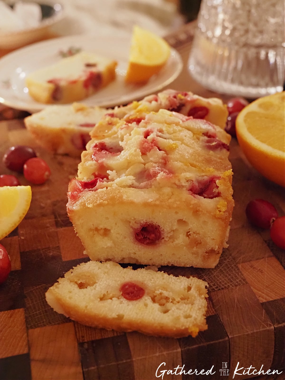 Mini loaf of cranberry orange pound cake on a wooden cutting board with sliced pieces, fresh cranberries, and orange slices, a festive Christmas bread and homemade baked good for neighbor gifts | Gathered In The Kitchen