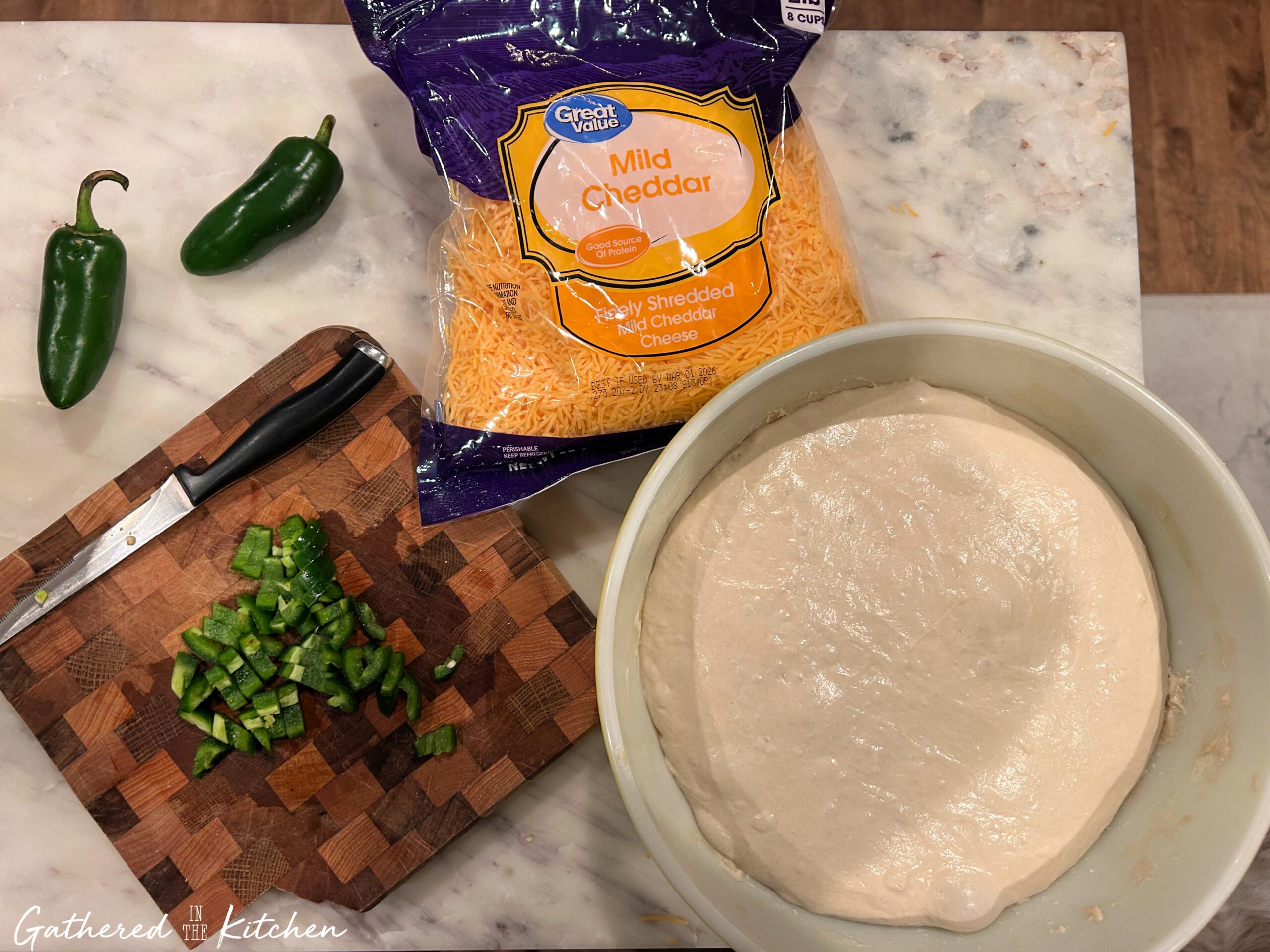 Sourdough bread dough in a bowl with chopped jalapeños and shredded cheddar cheese prepared as inclusions | Gathered In The Kitchen