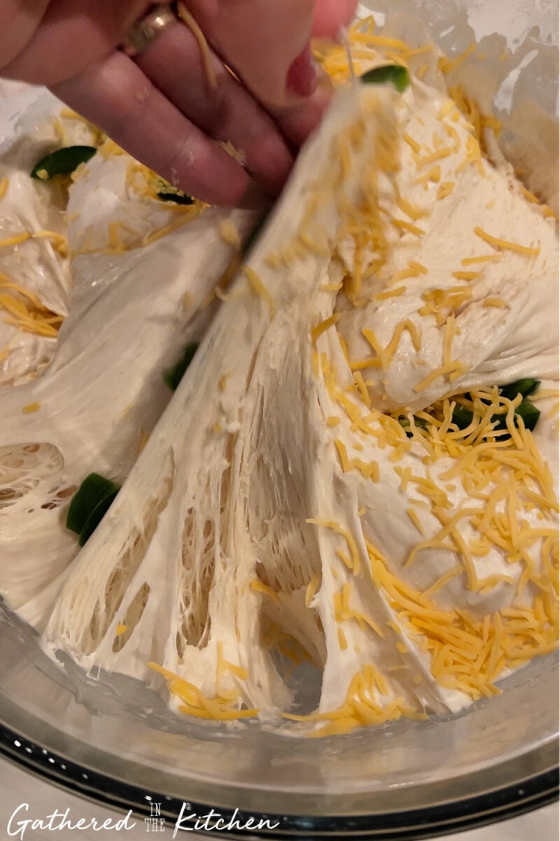 Hand stretching sourdough dough while folding in shredded cheese and sliced jalapeños | Gathered In The Kitchen 