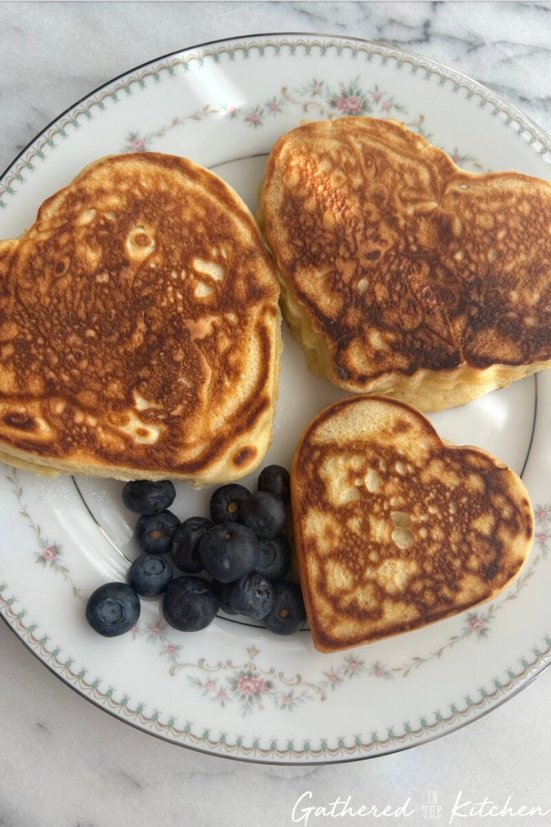 Heart-shaped pancakes served on a plate with fresh blueberries. | Gathered In The Kitchen 