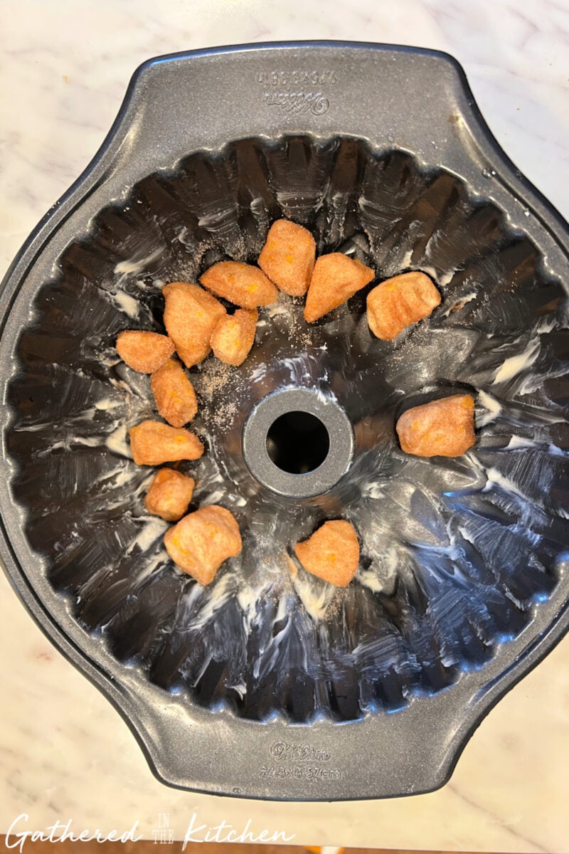 Cinnamon sugar coated biscuit pieces layered in a Bundt pan for monkey bread. | Gathered In The Kitchen 