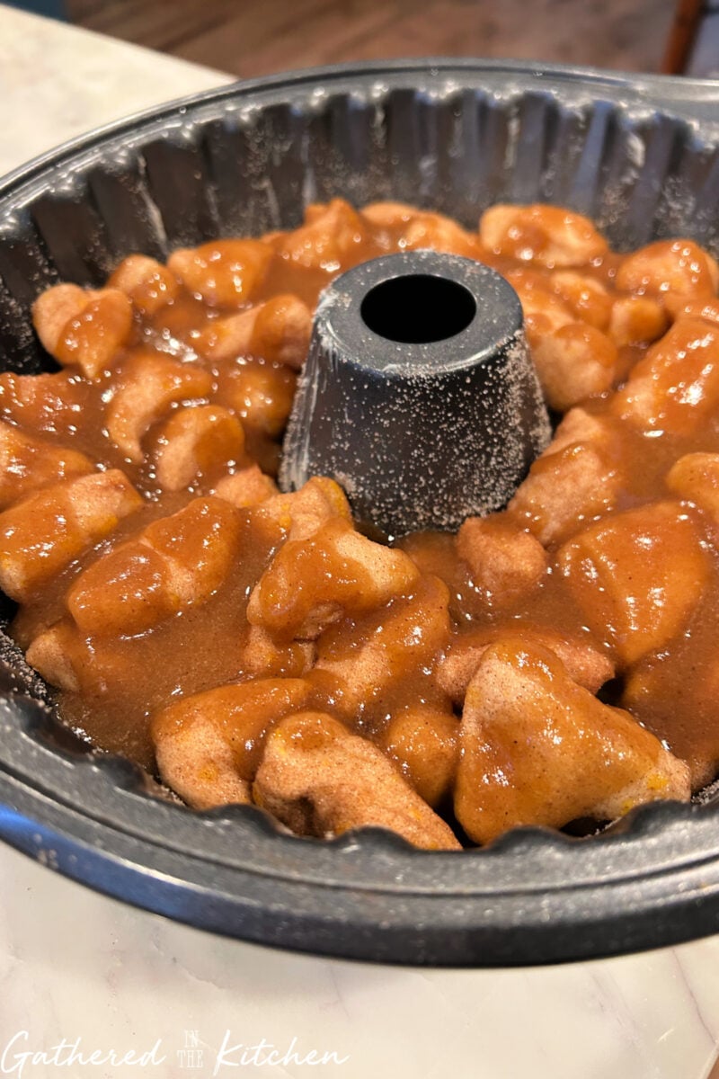 Close-up of biscuit dough coated in cinnamon sugar and caramel glaze before baking. | Gathered In The Kitchen 