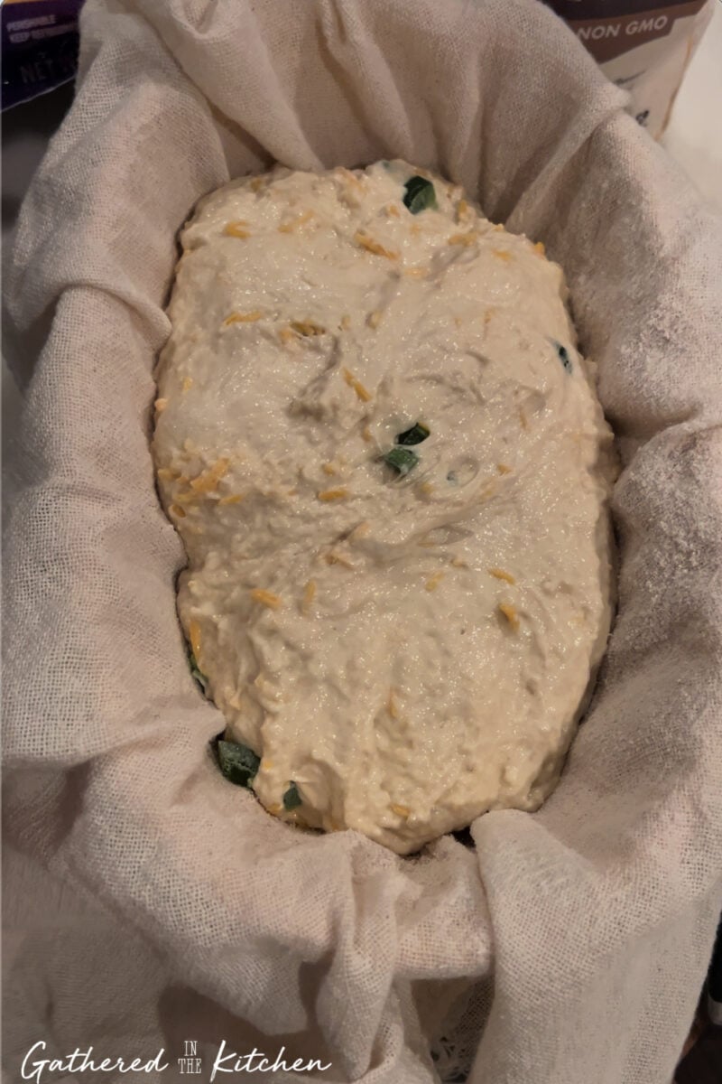 Shaped sourdough dough with cheese and jalapeños resting in a cloth-lined banneton basket before cold proofing in the refrigerator | Gathered In The Kitchen