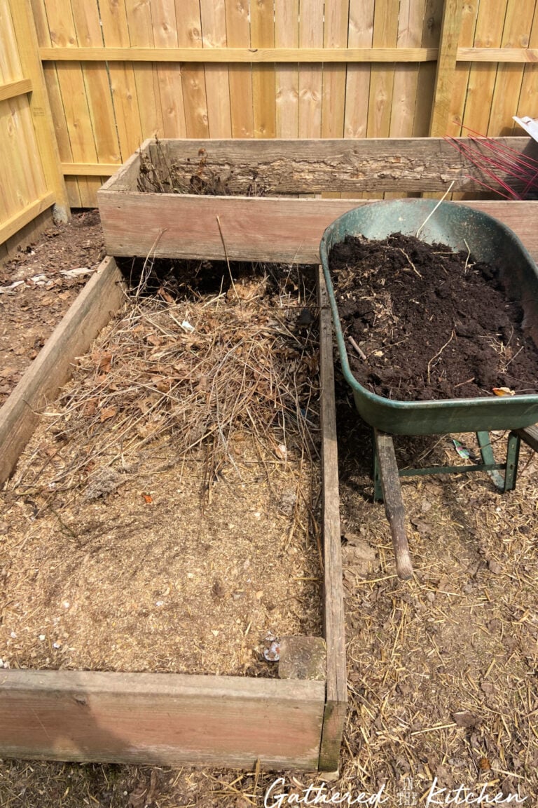 Raised garden bed being filled with organic yard waste and compost during spring garden cleanup to build healthy soil for planting.