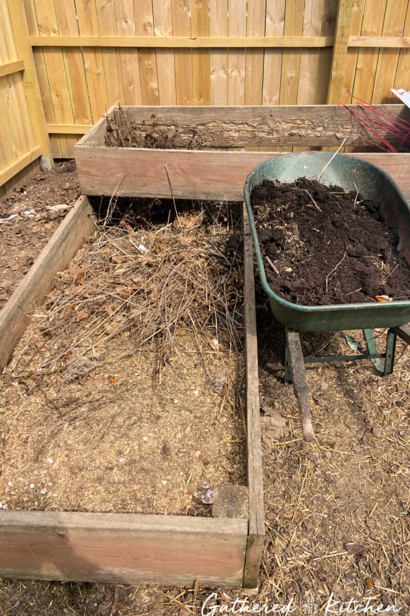 Raised garden bed being filled with organic yard waste and compost during spring garden cleanup to build healthy soil for planting.