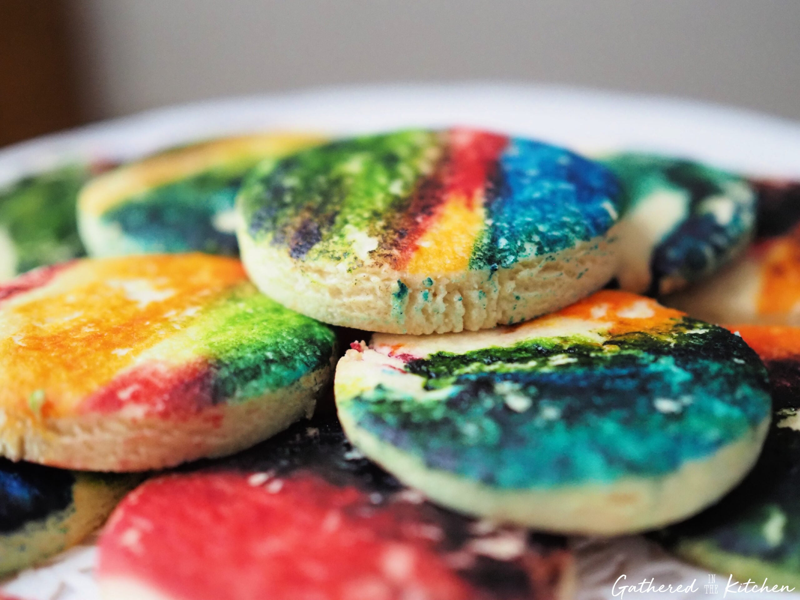 Plate of tie dye sugar cookies with colorful marbled patterns on a white plate on a marble countertop | Gathered In The Kitchen