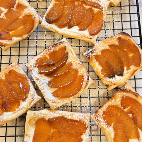 Baked spiced peach goat cheese danishes on a cooling rack dusted with powdered sugar | Gathered In The Kitchen