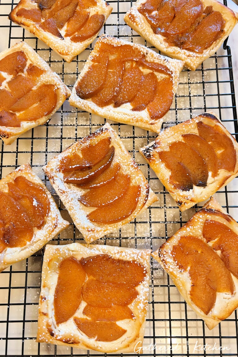 Baked spiced peach goat cheese danishes on a cooling rack dusted with powdered sugar | Gathered In The Kitchen