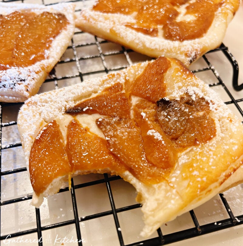 Close up of a spiced peach goat cheese danish with a bite taken out, showing flaky puff pastry layers and creamy filling | Gathered In The Kitchen 