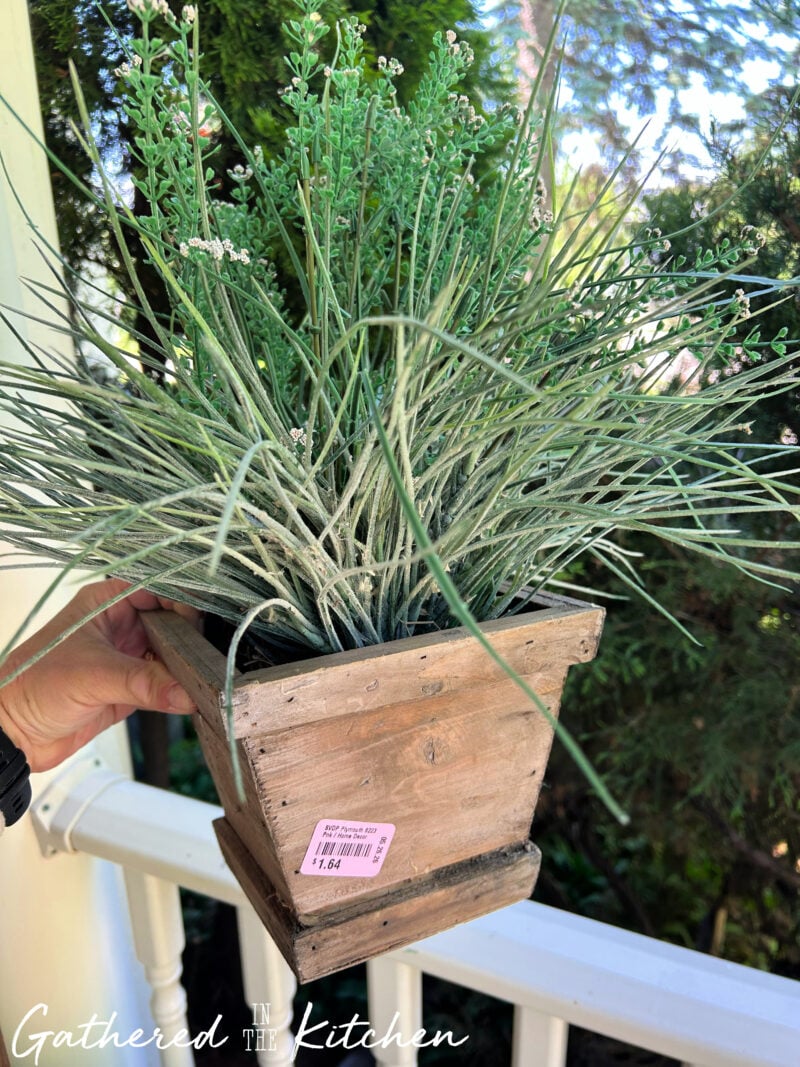Realistic faux grass and greenery arrangement in a rustic wooden planter purchased from a thrift store for $1.64. This budget-friendly thrifted planter was used to add texture and greenery to a patriotic front porch display. | Gathered In The Kitchen 