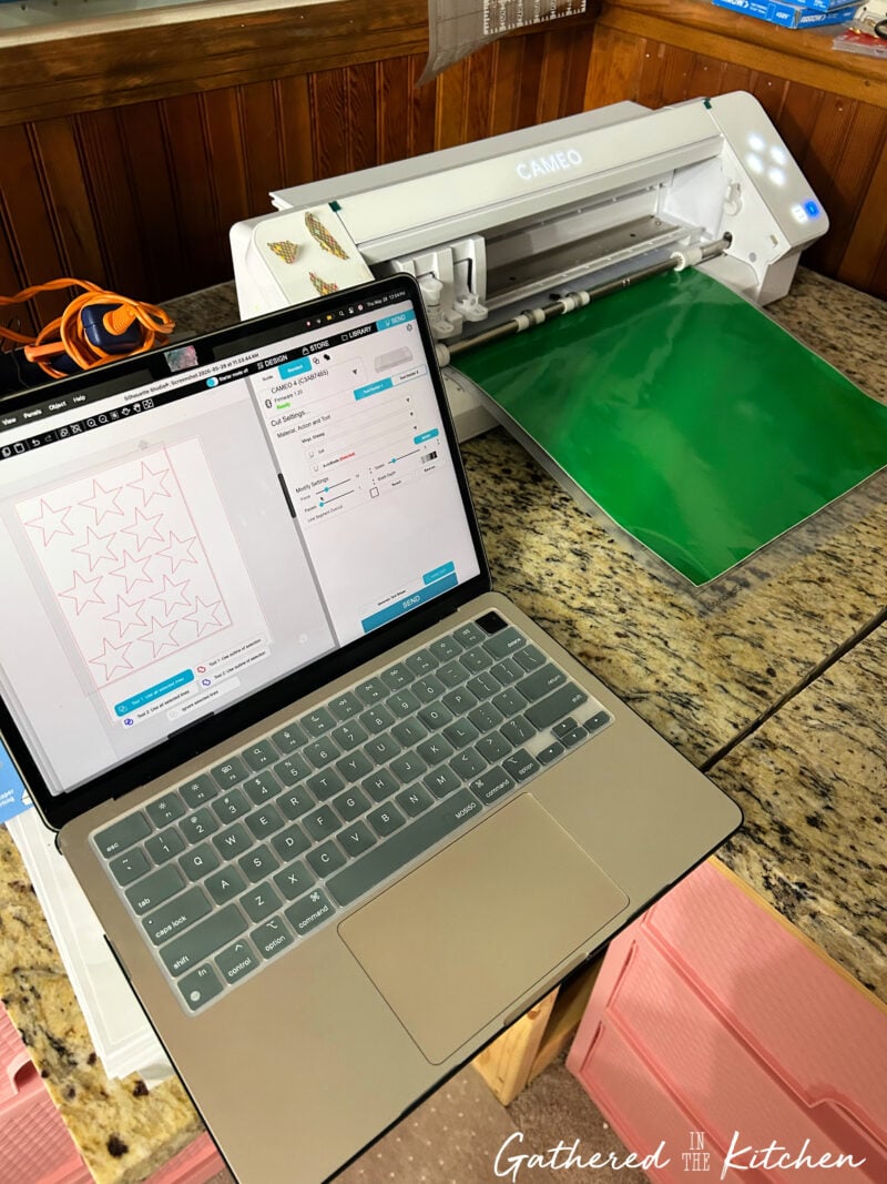 Silhouette Cameo cutting star-shaped vinyl stencils on green vinyl for a DIY patriotic wooden porch sign featuring an Americana-inspired American flag design. | Gathered In The Kitchen 