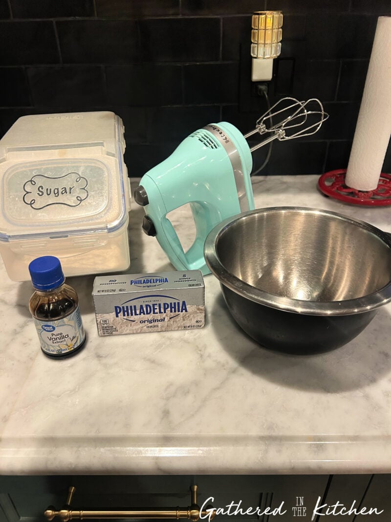 Cream cheese, vanilla extract, sugar, mixing bowl and hand mixer arranged on a kitchen counter for making cream cheese fruit dip. | Gathered In The Kitchen 