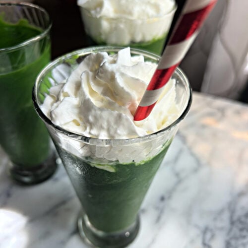 Green spinach and pineapple smoothie topped with whipped cream and served with a red and white striped straw | Gathered In The Kitchen