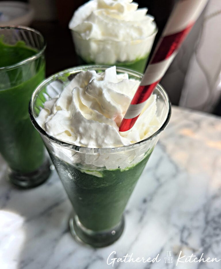 Green spinach and pineapple smoothie topped with whipped cream and served with a red and white striped straw | Gathered In The Kitchen