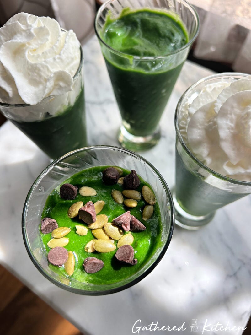 Green pineapple spinach smoothies topped with whipped cream, salted pumpkin seeds and chocolate chips | Gathered In The Kitchen