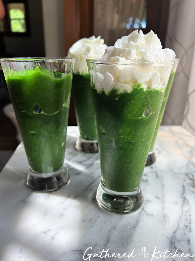 Four glasses of thick green spinach and pineapple smoothies, with two topped with whipped cream | Gathered In The Kitchen